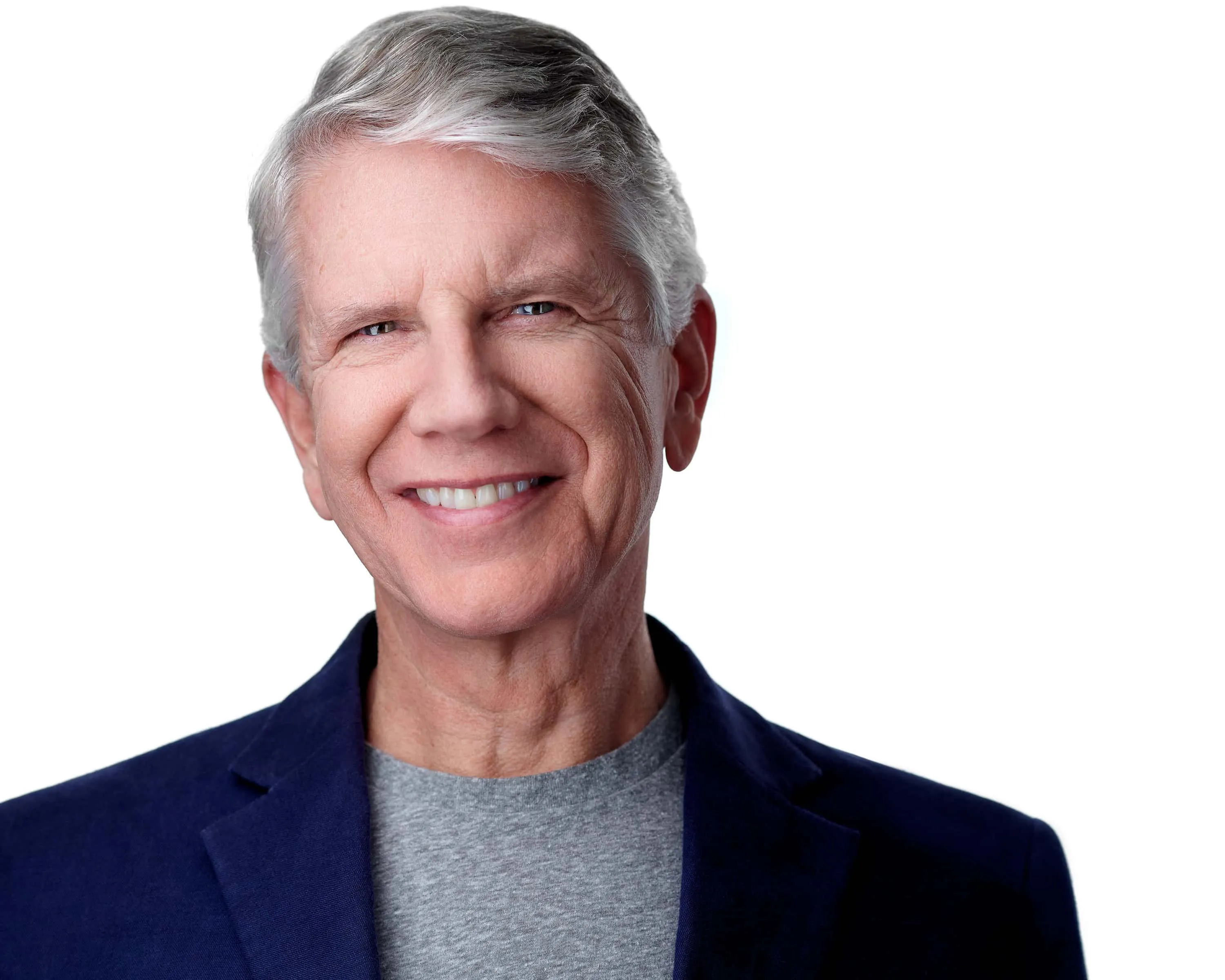 Professional business headshot of man with short silver-gray styled hair with side part and bright white smile wearing navy blue textured blazer over heather gray crew neck t-shirt photographed against seamless white studio background with directional key fill kick lighting technique by Richard Waine Lancaster Pennsylvania