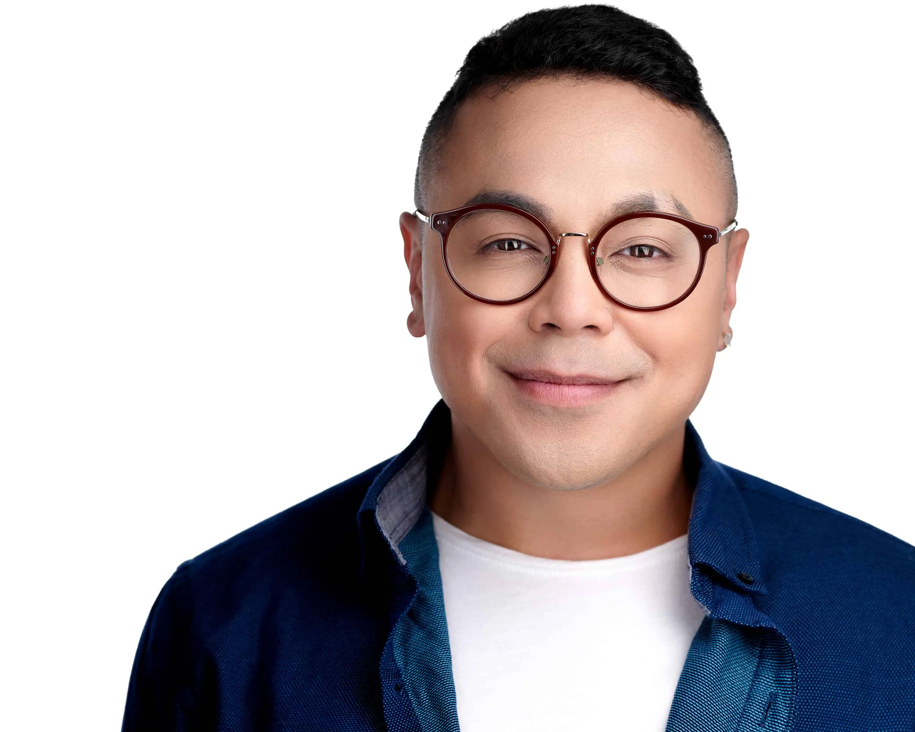 Man with round burgundy eyeglasses in unbuttoned navy shirt over white tee photographed on seamless white studio background
