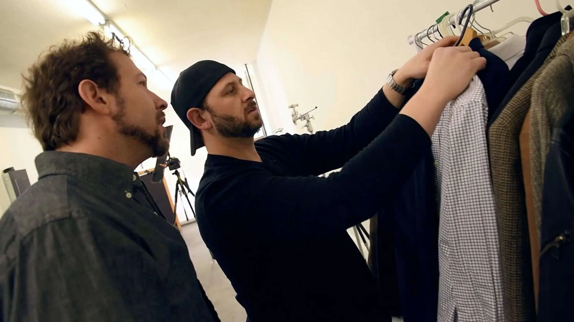 Photographer in black cap helping client select clothing from wardrobe rack in Lancaster PA photography studio