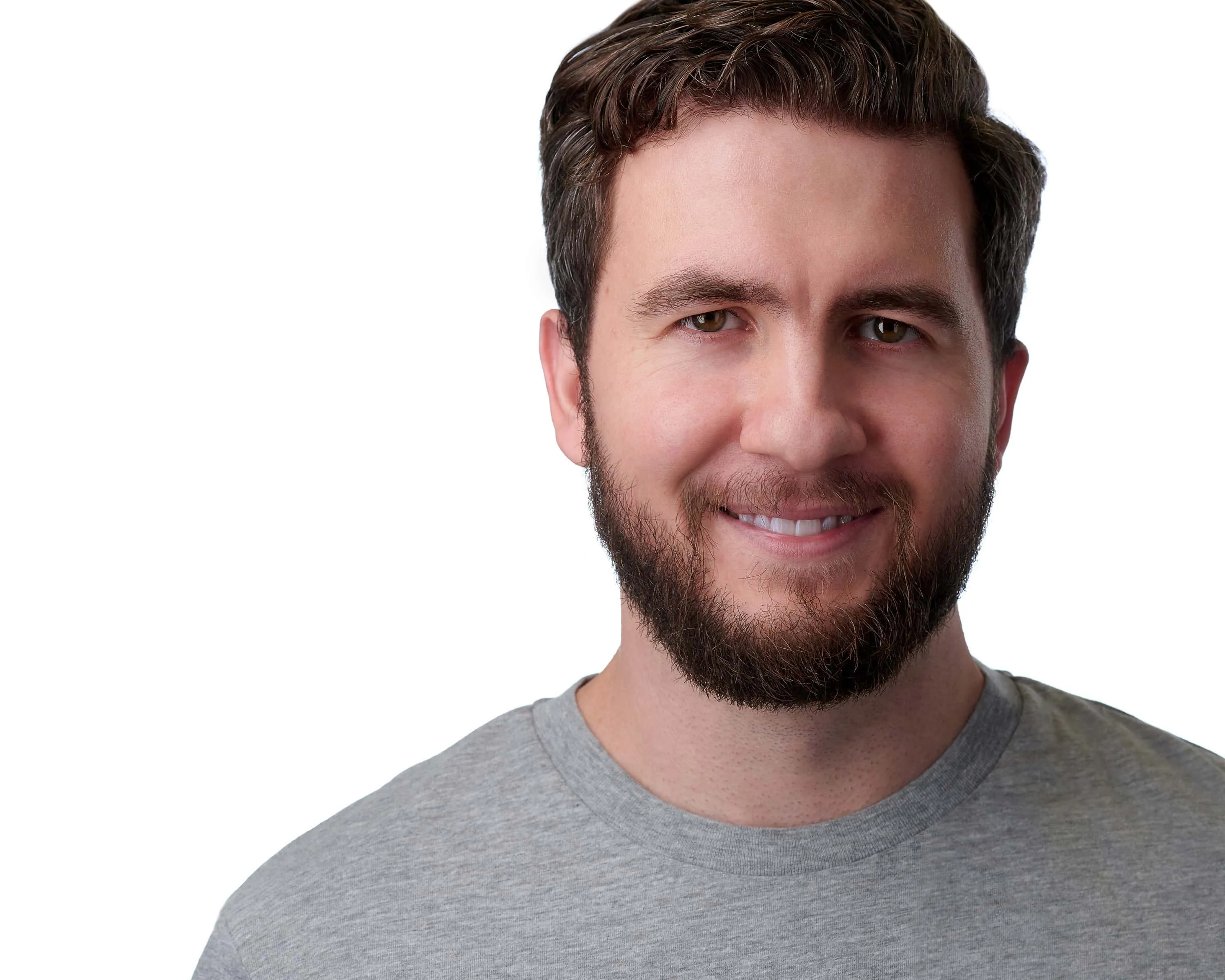 Professional headshot of male with short brown wavy hair, full brown beard, bright white smile showing teeth, wearing grey crew neck t-shirt, photographed on seamless white background in Lancaster, Pennsylvania by headshot photographer Richard Waine