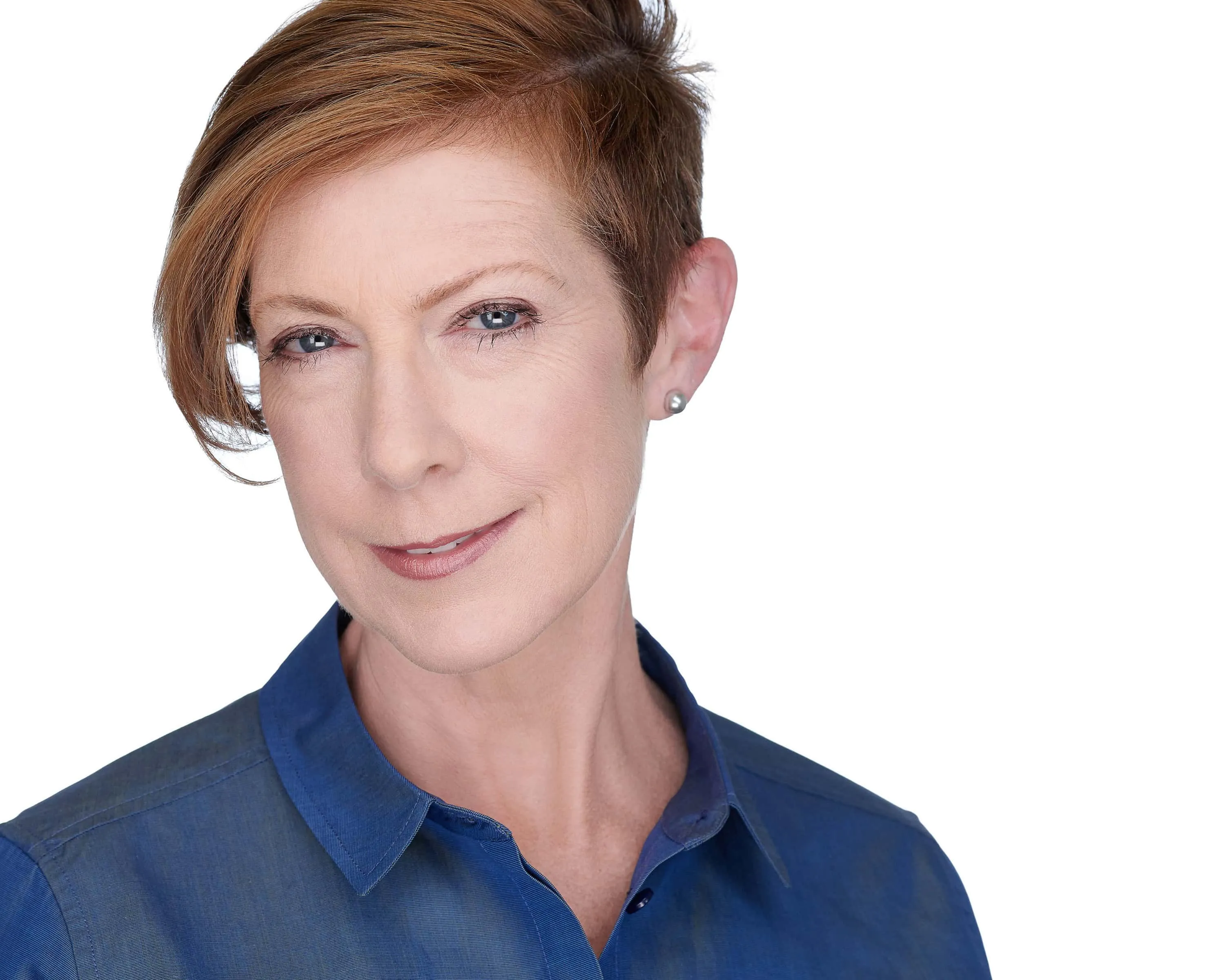 Professional headshot of female with short auburn brown pixie cut hairstyle, silver pearl stud earrings, wearing navy blue collared button-down shirt, photographed on seamless white background in Lancaster, Pennsylvania by headshot photographer Richard Waine