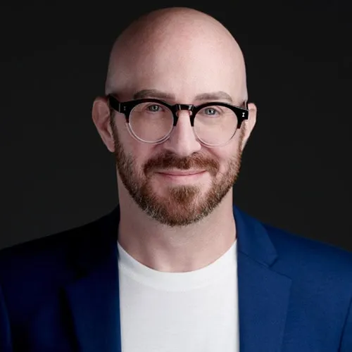 Professional linkedin profile headshot of bald man with short reddish-brown beard and round dark-framed glasses wearing navy blue blazer over white crew neck shirt against dark studio background by Richard Waine Photography Lancaster PA