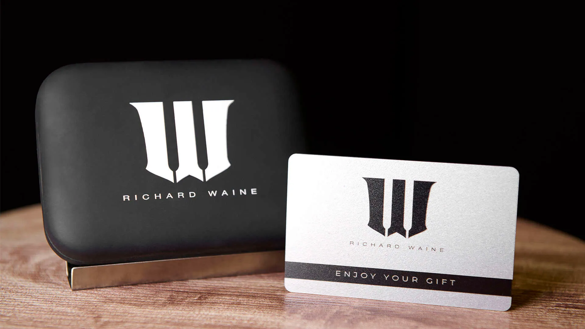 Product photograph of Richard Waine Photography branded gift card and hard shell case featuring white business logo on black rounded rectangular storage case with silver metallic gift card displaying black business logo and text Enjoy Your Gift on wooden surface by Richard Waine Photography Lancaster Pennsylvania