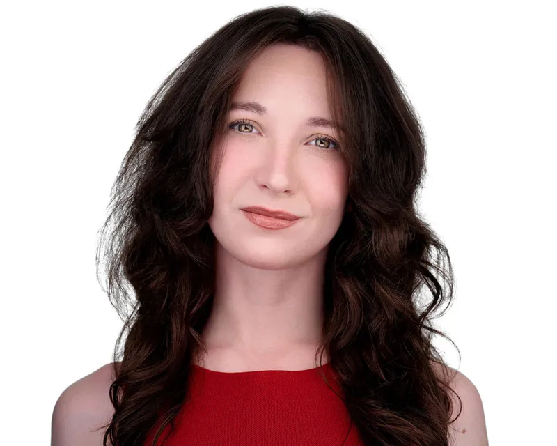 Professional performer headshot of woman with long voluminous dark brown wavy hair with caramel highlights styled with a part and soft natural makeup wearing vibrant red sleeveless textured knit shell top photographed against seamless white studio backdrop with high-key professional studio lighting by Richard Waine professional headshot photographer serving Lancaster York Hershey Pennsylvania Baltimore Maryland