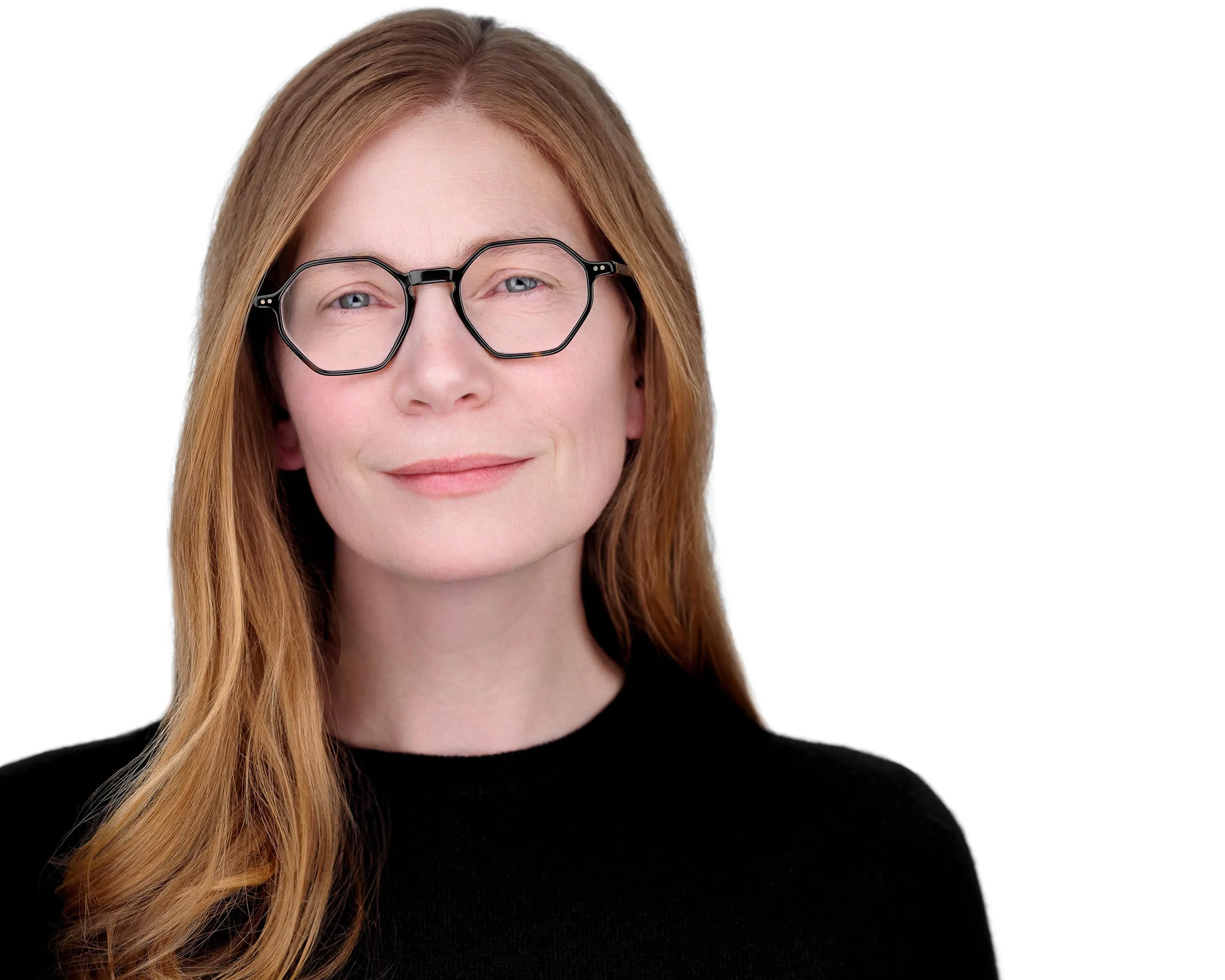 Professional headshot of female with long straight strawberry blonde hair, wearing black hexagonal frame eyeglasses and black crew neck top, subtle smile, photographed on seamless white background in Lancaster, Pennsylvania by headshot photographer Richard Waine