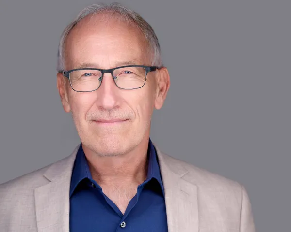 Professional headshot of attorney in tan blazer over navy dress shirt projecting authority and competence against neutral gray studio background by Richard Waine Photography