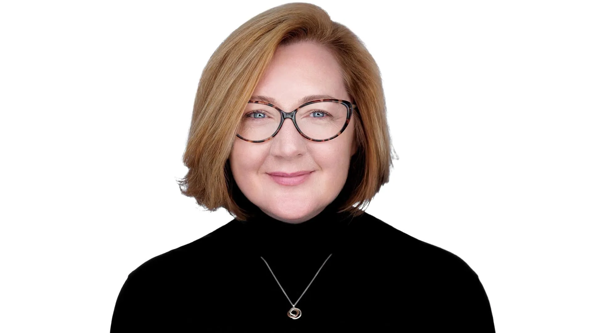 Professional headshot of female with shoulder-length brown bob hairstyle, wearing brown oval frame eyeglasses and black turtleneck with silver pendant necklace, warm smile, photographed on seamless white background in New York City, New York by headshot photographer Richard Waine