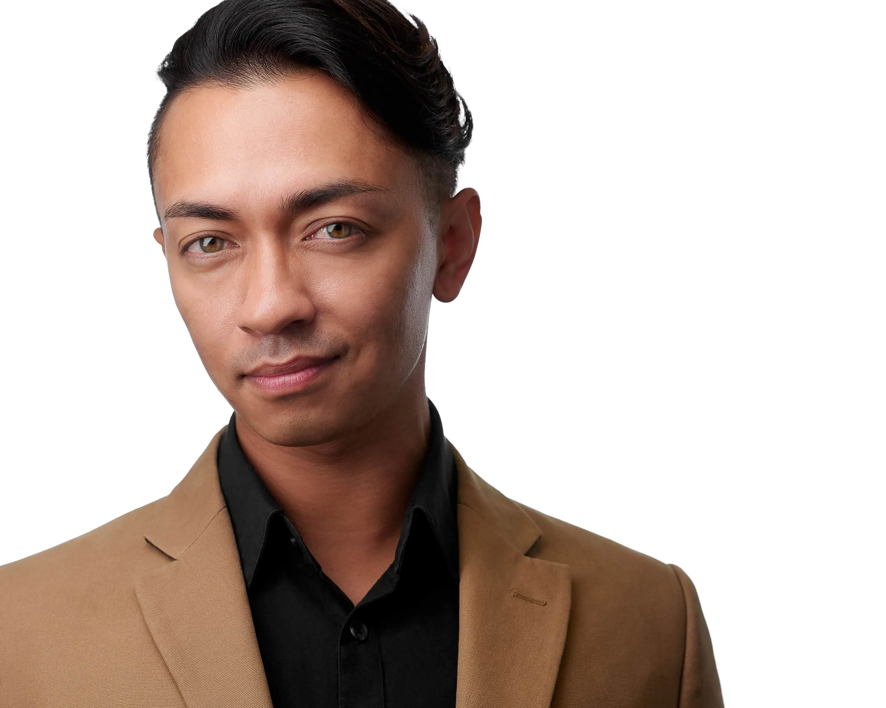 Professional headshot of male makeup artist with short black hair styled back, wearing tan blazer over black collared shirt, subtle smile, photographed on seamless white background in Lancaster, Pennsylvania by headshot photographer Richard Waine