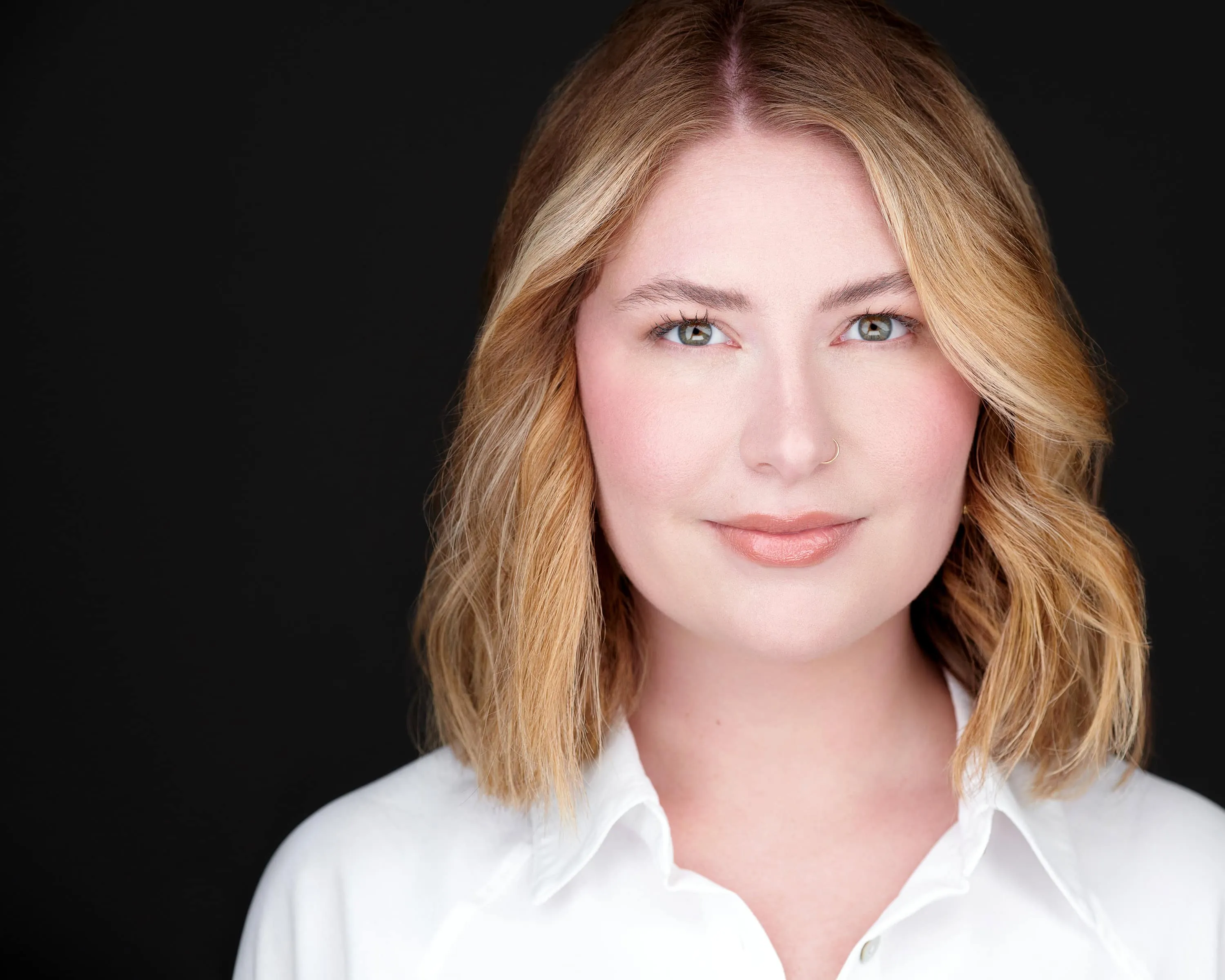 Professional corporate headshot of woman with textured wavy shoulder-length blonde hair with subtle highlights wearing crisp white collared button-down shirt photographed against rich black studio background with professional lighting by Richard Waine Photography Lancaster Pennsylvania