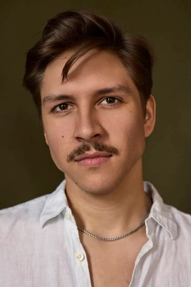 Professional portrait by Pete Coco Photography of male with styled dark brown hair swept back, trimmed brown mustache, wearing white linen button-down shirt with silver chain necklace, photographed against warm brown olive gradient background with dramatic Rembrandt lighting, New York portrait photography example