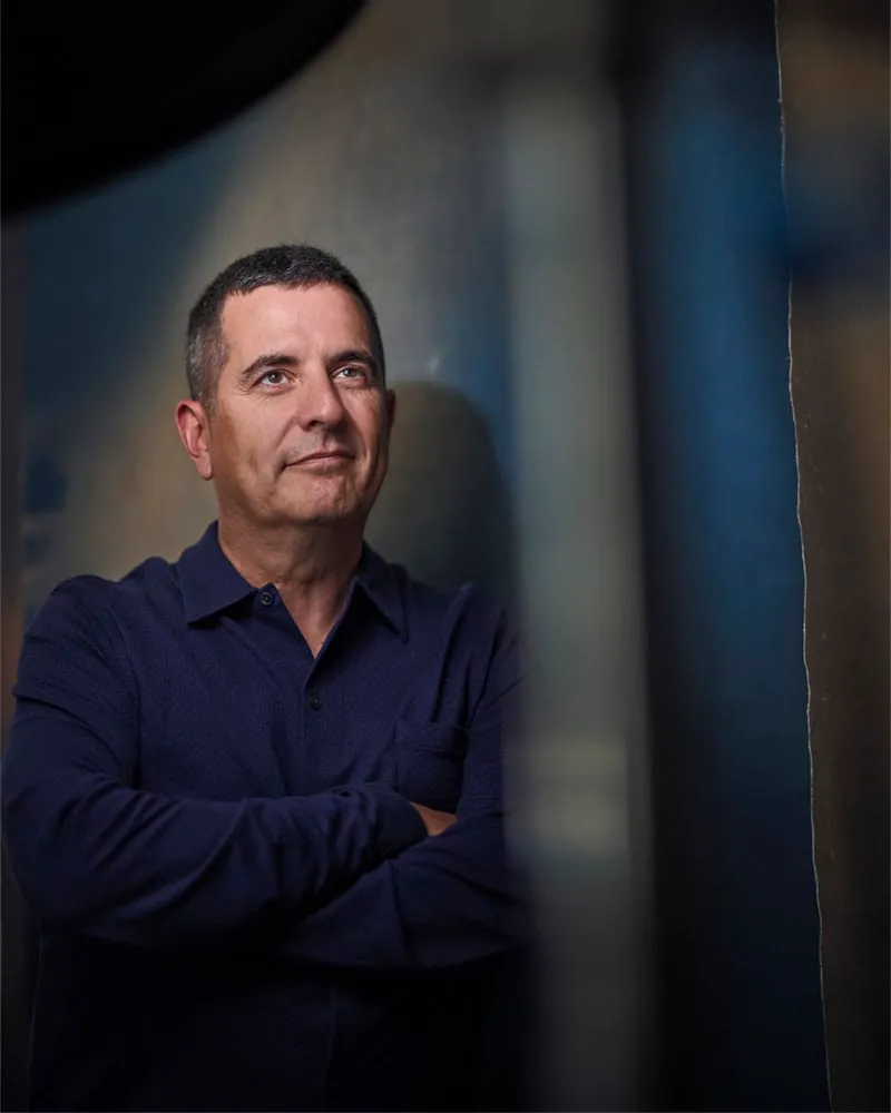 Professional portrait by Pete Coco Photography of male with short dark brown hair, trimmed beard, wearing navy blue collared polo shirt, arms crossed, photographed against layered canvas backgrounds, New York portrait photography example