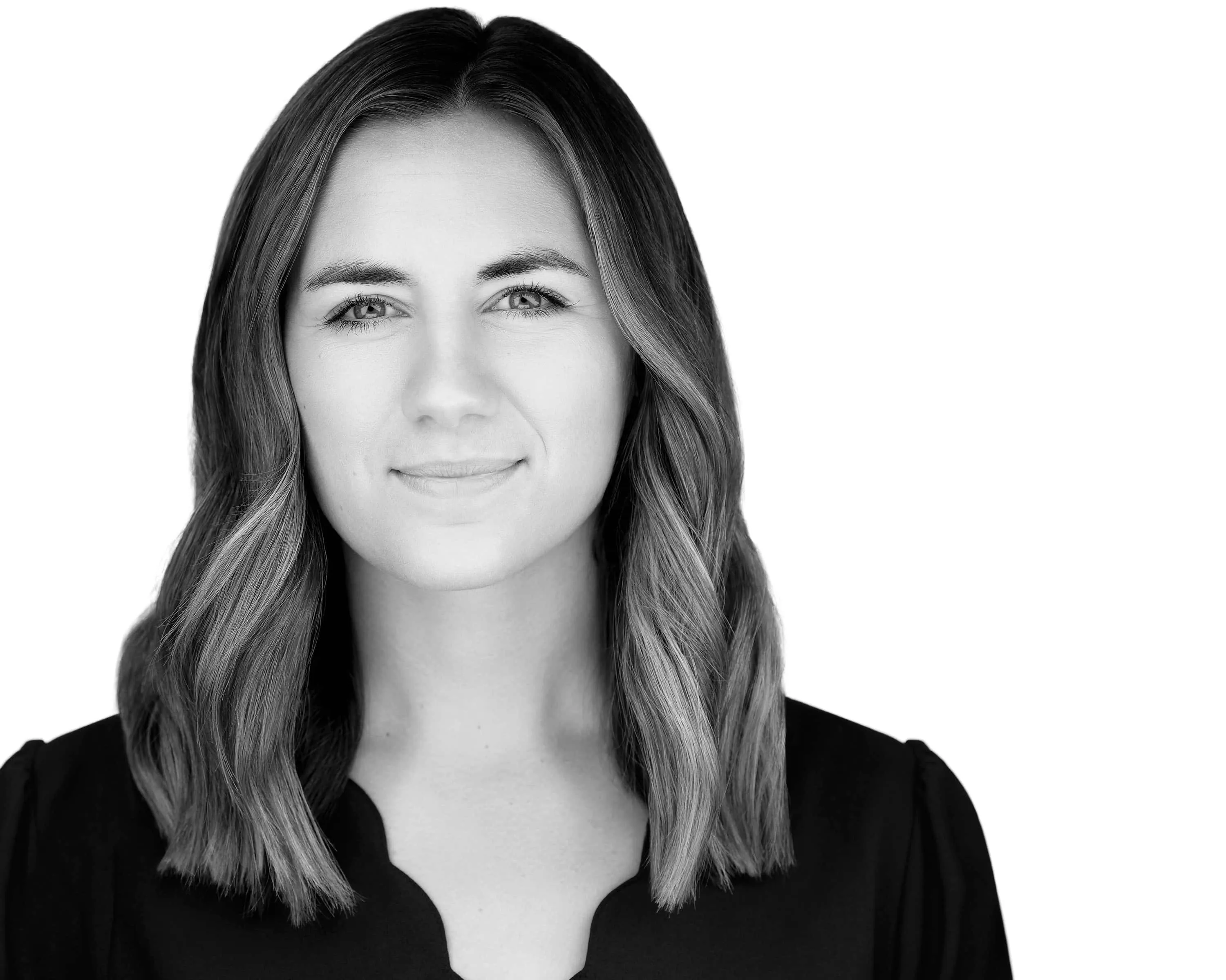 Professional black and white headshot of young Caucasian woman with shoulder-length wavy hair with side part wearing black top showing confident approachable expression with natural subtle closed-mouth smile photographed against seamless white background with professional high-key lighting by Richard Waine Photography Lancaster Pennsylvania