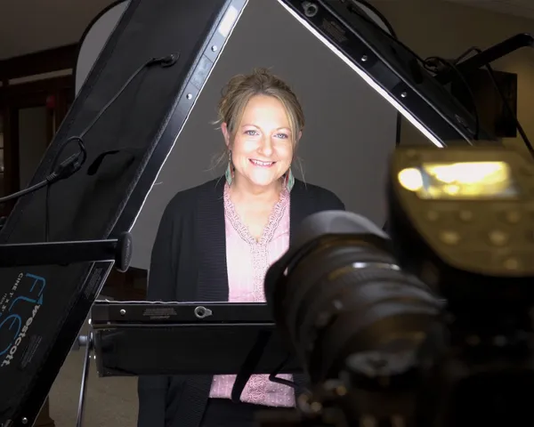 Behind-the-scenes professional linkedin profile headshot photography session showing woman in black cardigan and pink lace top positioned between Westcott lighting panels and camera by Richard Waine