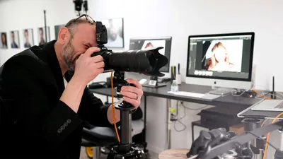 Professional headshot photographer Richard Waine photographing a business professional in Lancaster PA studio with dual monitor setup displaying corporate headshots