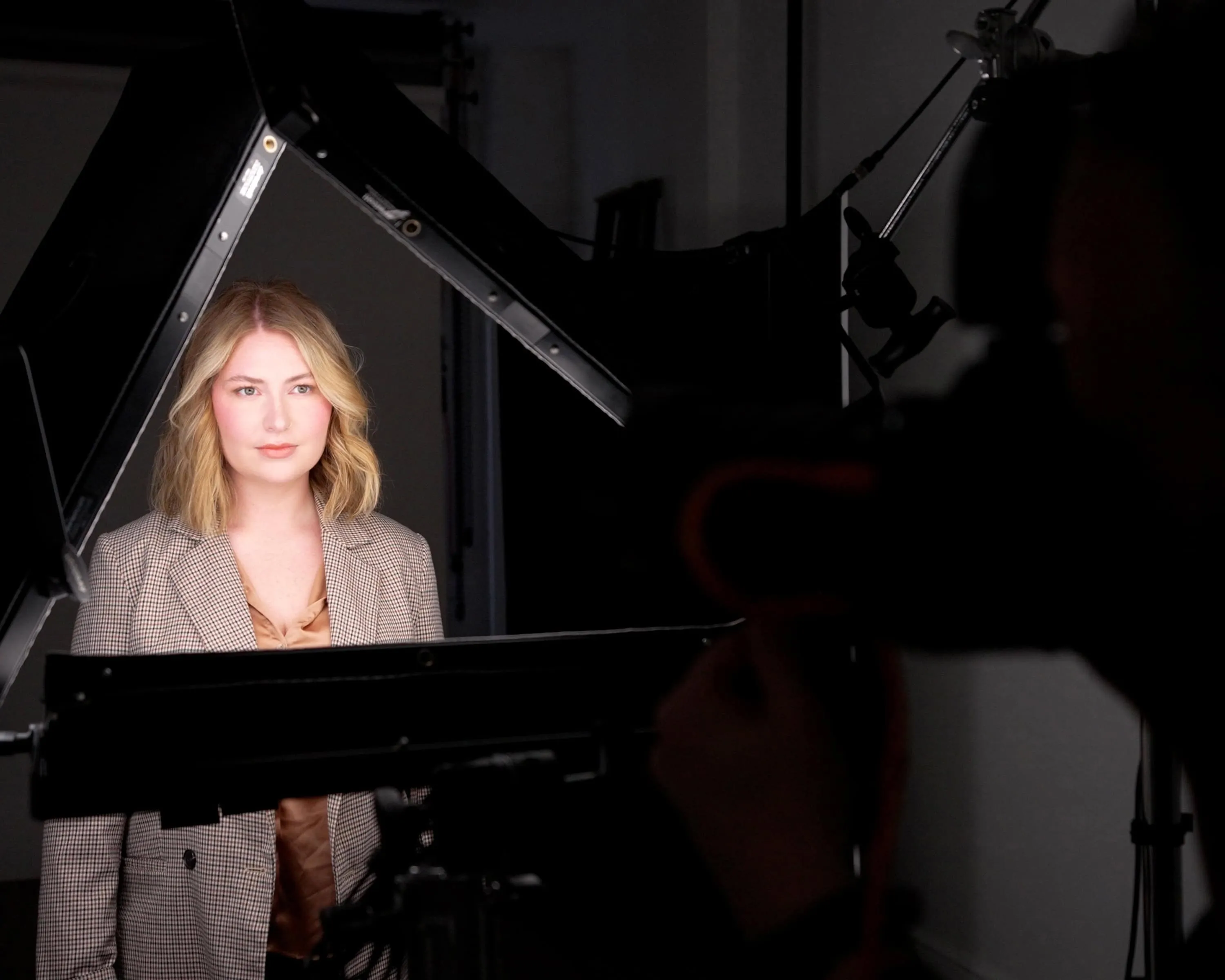 Behind-the-scenes view of female client in brown and tan houndstooth blazer over rust-colored blouse positioned between large black rectangular studio lighting panels and modifiers during professional headshot session at Richard Waine Photography Lancaster Pennsylvania