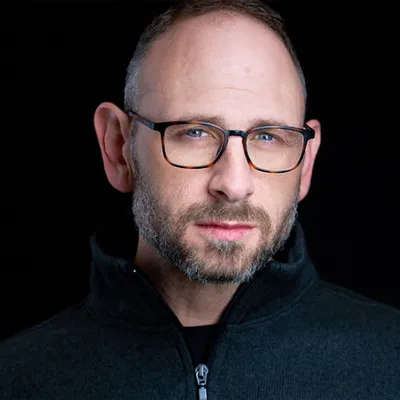 Professional headshot of Richard Waine Lancaster Pennsylvania headshot photographer with short brown hair receding hairline and trimmed brown and gray beard wearing tortoise-shell frame eyeglasses and dark gray quarter-zip fleece pullover photographed against black studio background with dramatic studio lighting by colleague photographer Sanjeev Singhal