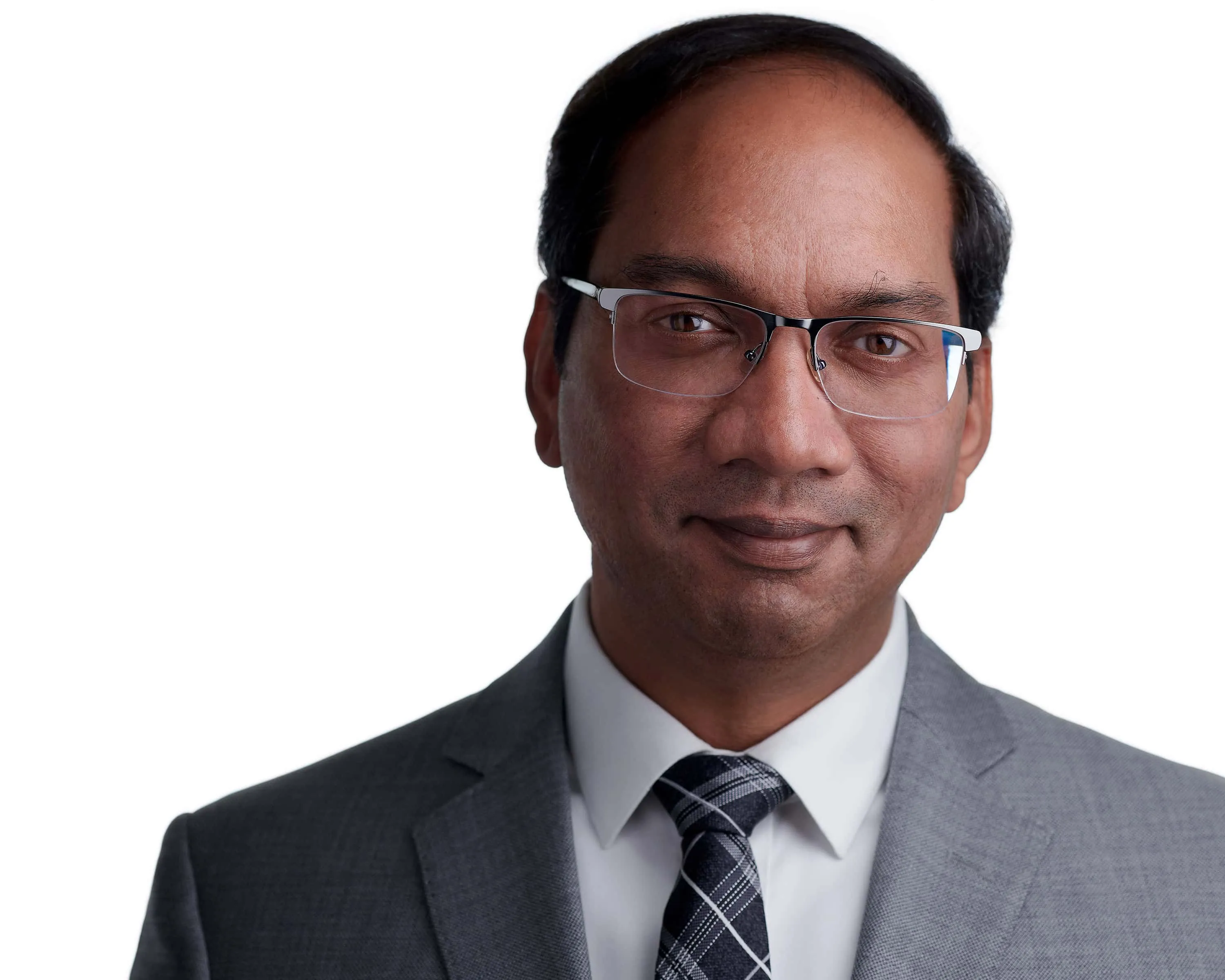 Male professional headshot with short black hair, rectangular frame eyeglasses, wearing grey suit jacket over white dress shirt with grey black and white checkered tie, photographed on seamless white background by Lancaster Pennsylvania headshot photographer Richard Waine
