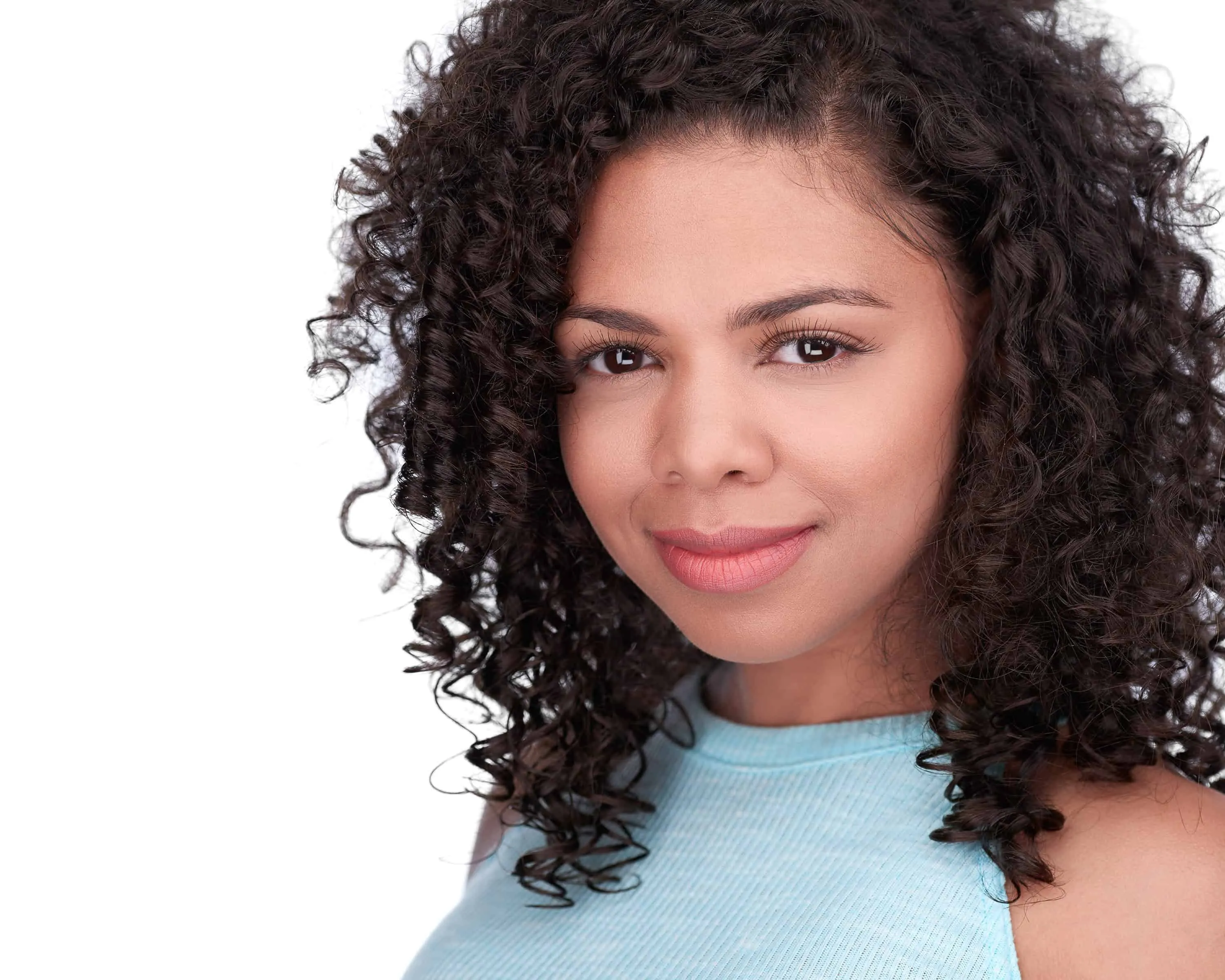 Woman with voluminous dark curly hair wearing light blue top against white studio background with bright smile