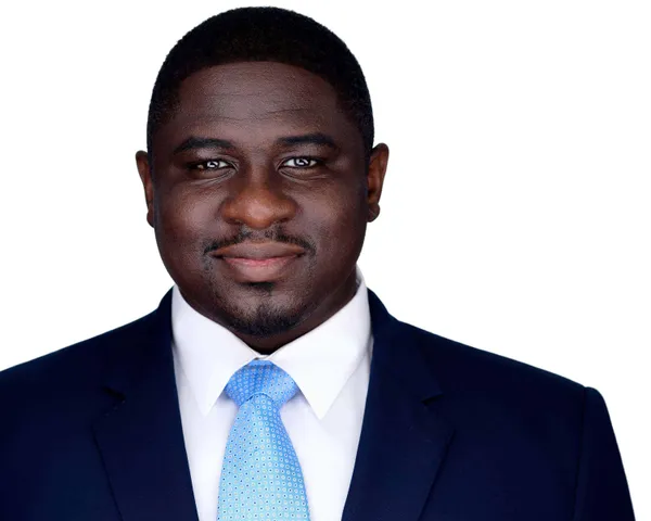 Professional business headshot of African-American man with short hair and goatee wearing navy blue suit with light blue patterned tie on white studio background by Richard Waine Photography